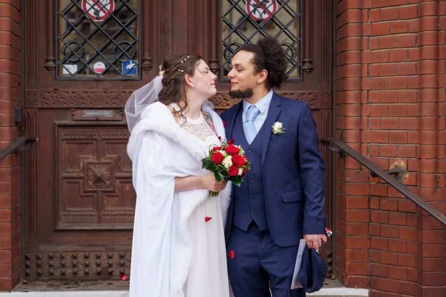 Hochzeitspaar vor dem Standesamt Rathaus Lichtenberg, Braut in weißem Kleid und Bräutigam in blauem Anzug.